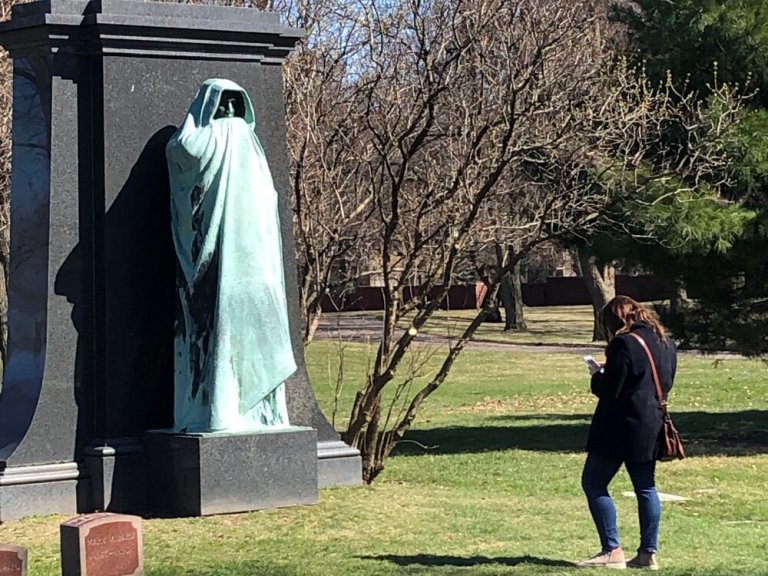 A masked visitor to Graceland Cemetery in Chicago pays homage to Lorado Taft’s sculpture “Eternal Silence” early on in the pandemic. (One Illinois/Ted Cox)